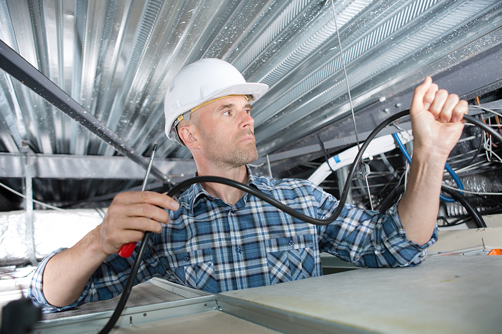 An expert technician runs network cables through the roof of an office